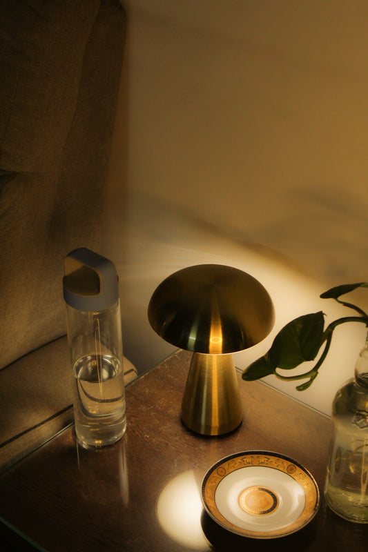 Gold lamp on a table with a glass of water and a plant in a dimly lit room